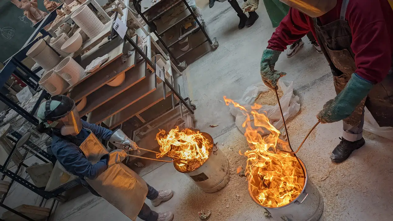 Personas con equipo de protección manipulando piezas incandescentes de cerámica durante una cocción rakú.